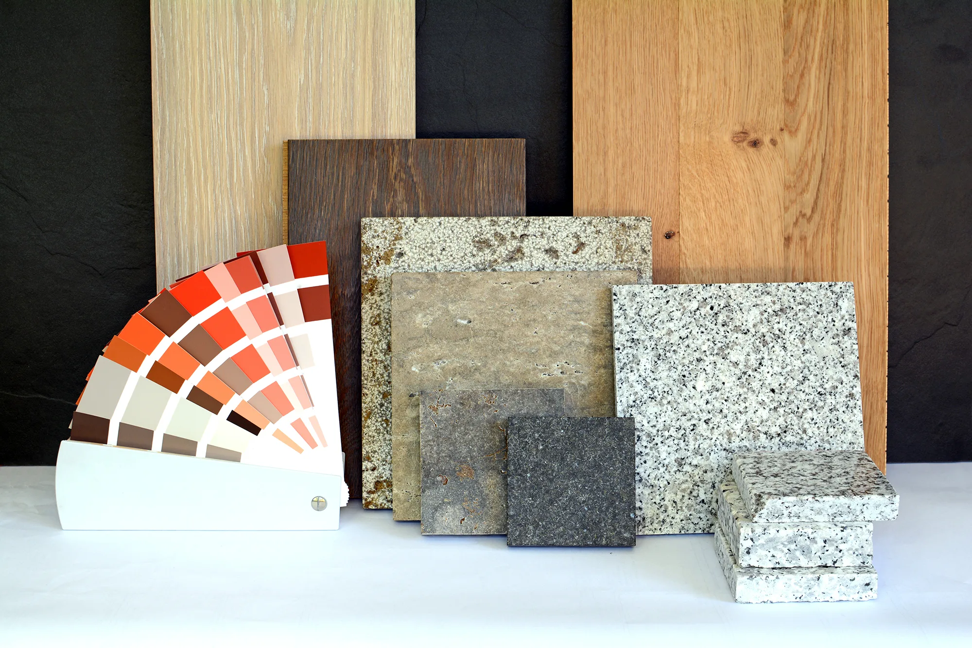 A display of wood panels, granite and stone tiles, and a range of colors in neutral and earthy tones, all arranged on a white background to provide inspiration for interior design or home staging.